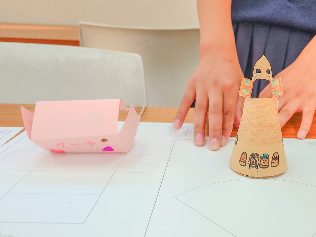 子どもがつくった紙のおうち。とんがり屋根のおうちに顔と住人が描かれている