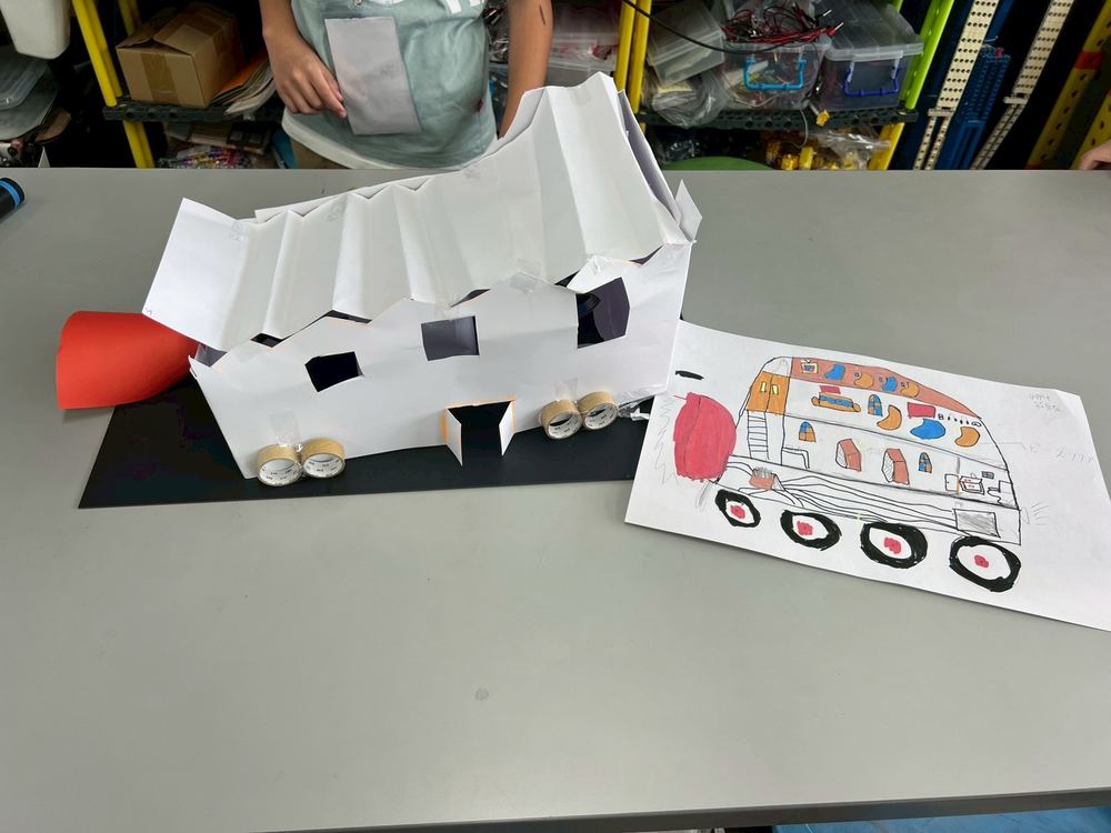 A bus-shaped library model with wheels, and its design drawing